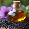 Flakon oleju z czarnuszki otoczony czarnymi nasionami i kwiatami Nigella sativa.